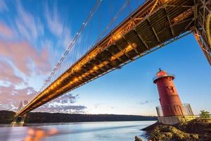 George Washington Bridge und der rote kleine Leuchtturm im Fort Washington Park, New York, New York am Abend. foto