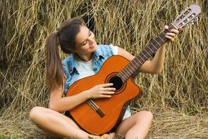 Junge und glückliche Frau, die im Dorf Gitarre spielt foto