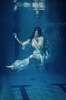 Frau, die ein schönes Kleid unter Wasser in einem Schwimmbad trägt foto