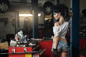 Mechanikerin in der Garage mit künstlerischem Make-up im Gesicht, stilisiert wie ein schmutziger Fleck foto