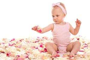 süßes Babymädchen sitzt umgeben von Rosenblättern foto