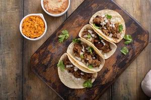 Schweinefleisch-Carnitas-Tacos mit Zwiebeln und Koriander, serviert mit Reis und Bohnenmus foto