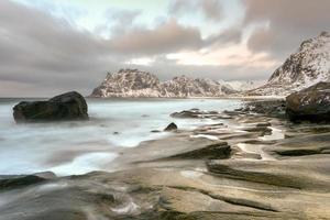 Wellen, die im Winter über den Strand von Utakleiv, Lofoten, Norwegen fließen. foto