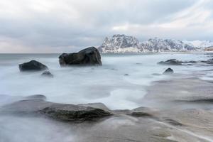 Wellen, die im Winter über den Strand von Utakleiv, Lofoten, Norwegen fließen. foto