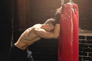 Kämpfer ist während seines Trainings mit einem Boxsack sehr müde foto