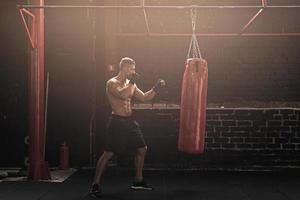 starker junger MMA-Kämpfer und roter Boxsack foto