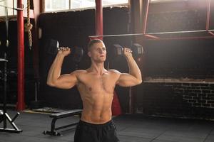 junger gutaussehender bodybuilder, der schulterpresse im cross-trainingsstudio macht foto