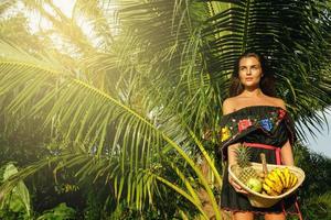 glückliche junge Frau mit einem Korb voller exotischer Früchte foto
