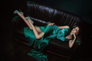 Model in schönem grünen Kleid posiert auf Ledercouch foto