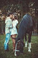 junges Paar in Umarmung auf der Wiese mit Pferden foto