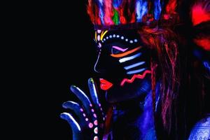 Modell im Bild des amerikanischen Ureinwohners mit Neon-Make-up, das aus fluoreszierender Farbe im ultravioletten Licht besteht. foto