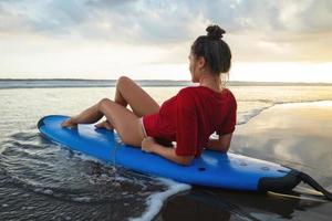 Frau, die nach ihrer Surfsession auf dem Surfbrett am Strand sitzt foto
