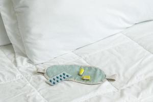 Ohrstöpsel, Augenbinde und Schlaftabletten auf dem Bett foto