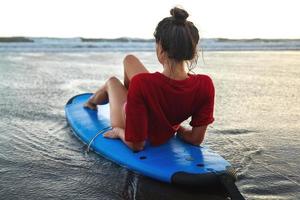 Frau, die nach ihrer Surfsession auf dem Surfbrett am Strand sitzt