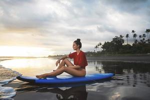 Frau, die nach ihrer Surfsession auf dem Surfbrett am Strand sitzt foto