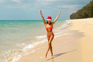 Frau mit Bikini und Weihnachtsmütze am Strand. Winterurlaub in den warmen Ländern. foto