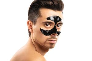 junger Mann mit einer schwarzen Holzkohlemaske auf seinem Gesicht auf weißem Hintergrund. foto