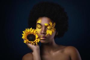 afrikanische frau mit einer sonnenblume und kreativem make-up auf ihrem gesicht foto