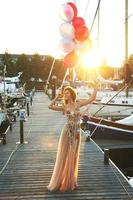 Frau in schönem Kleid mit vielen bunten Luftballons auf dem Yachtpier foto