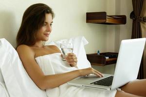 Frau liegt auf dem Bett und benutzt Laptop-PC foto