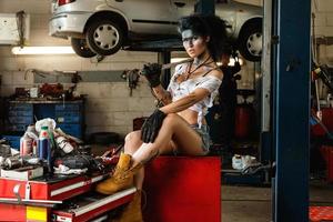 Mechanikerin in der Garage mit künstlerischem Make-up im Gesicht, stilisiert wie ein schmutziger Fleck foto