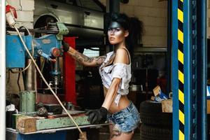 Mechanikerin in der Garage mit künstlerischem Make-up im Gesicht, stilisiert wie ein schmutziger Fleck foto