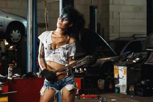 Mechanikerin in der Garage mit künstlerischem Make-up im Gesicht, stilisiert wie ein schmutziger Fleck foto