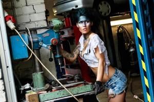 Mechanikerin in der Garage mit künstlerischem Make-up im Gesicht, stilisiert wie ein schmutziger Fleck foto