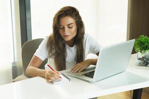 junge schöne Frau, die im Büro am Laptop-PC arbeitet foto