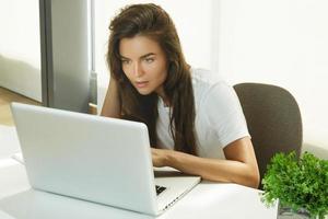 junge schöne Frau, die im Büro am Laptop-PC arbeitet foto