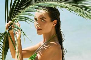 schöne Frau mit einem Palmblatt am Strand foto