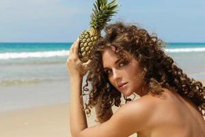 Frau mit einer Ananasfrucht am Strand foto