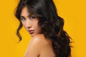 asiatische frau mit einem schönen lockigen haar und make-up auf gelbem hintergrund foto