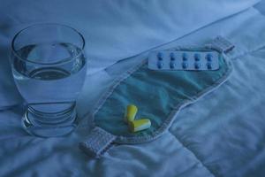 blisterpackung mit schlaftabletten, augenbinde und glas wasser foto