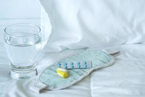 blisterpackung mit schlaftabletten, augenbinde und glas wasser foto