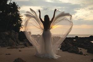 Silhouette der Braut, die ein wunderschönes Hochzeitskleid am Strand trägt foto