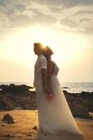 junges Ehepaar in Umarmung feiert ihre Hochzeit am Strand foto