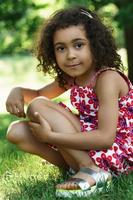 Kleines afrikanisches Mädchen, das auf einem Gras in einem Stadtpark sitzt foto