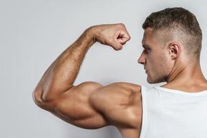 junger Bodybuilder, der seinen muskulösen Arm zeigt foto