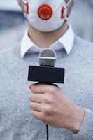 nachrichtenreporter, der eine präventionsmaske trägt und in ein mikrofon spricht foto