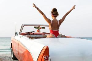 sexy Frau mit rotem Badeanzug sitzt in einem Retro-Cabriolet-Auto foto