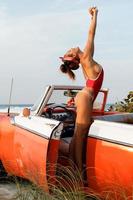 sexy Frau mit rotem Badeanzug im Retro-Cabriolet-Auto am Strand. foto