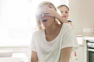 süßer junge bedeckt die augen seiner mutter in der küche foto