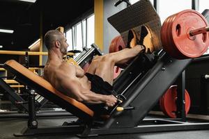 Bodybuilder, der eine sitzende Beinpresseübung in einem Fitnessstudio durchführt foto