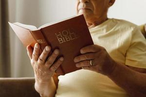 älterer mann, der zu hause die heilige bibel liest foto