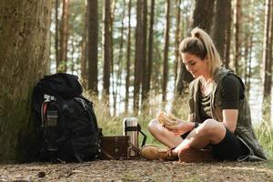 weibliche wanderer während des kleinen halts, der sandwich im grünen wald isst foto