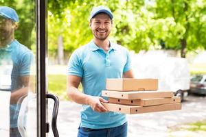 lächelnder Kurier während der Pizzalieferung in der Nähe eines Eingangs foto