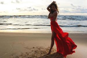 atemberaubende Frau, die ein wunderschönes rotes Kleid am Strand trägt foto