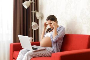 müde schwangere Frau sitzt mit einem Laptop-Computer foto