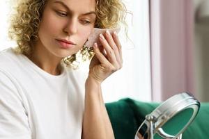 Frau, die Gesichtsmassage mit einem Rosen-Gua-Sha-Stein macht foto